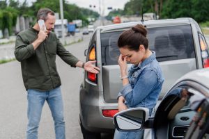 Upset man and woman near cars after car accident. This image answers the question why you need a car accident lawyer.