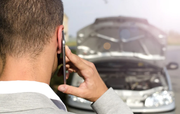 Person Calling On A Phone While Looking At A Damaged Car